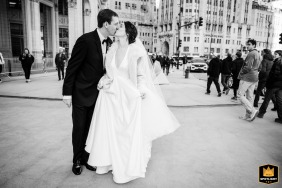 At the Wrigley Building in Chicago, IL, the bride and groom share a kiss while walking down the street.